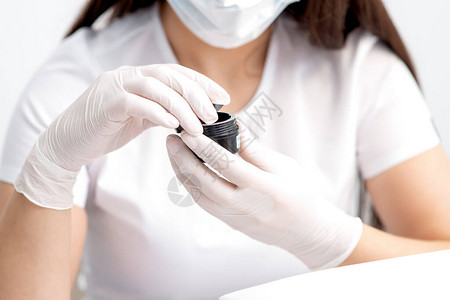带保护面罩的美容师或修甲大师用白手套将黑罐子和化妆品或指甲图片