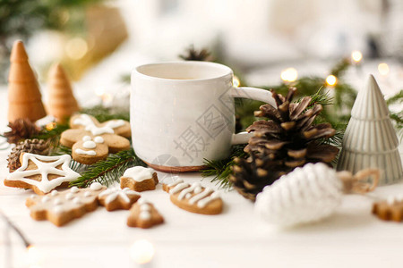 圣诞姜饼干时尚白杯咖啡松果和白色木制桌边的温暖灯光图片