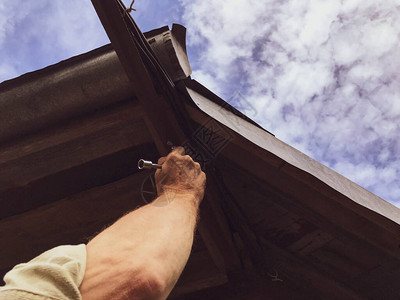 一名男子在高处用金属工具修理屋顶在木屋中制造屋顶填充住宅建筑中的孔洞图片