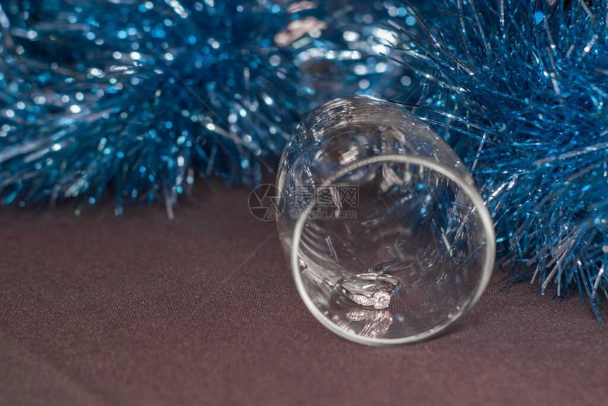 在一个香槟杯中订婚戒指在蓝色闪亮的圣诞树罐子附近图片