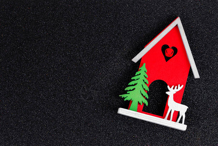 圣诞平面布局木制玩具屋一只鹿和一棵圣诞树在黑色闪发光的背景上圣诞贺卡图片