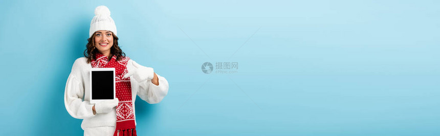 冬衣中快乐女人的丰收在数字平板上用手指着蓝色空白屏图片