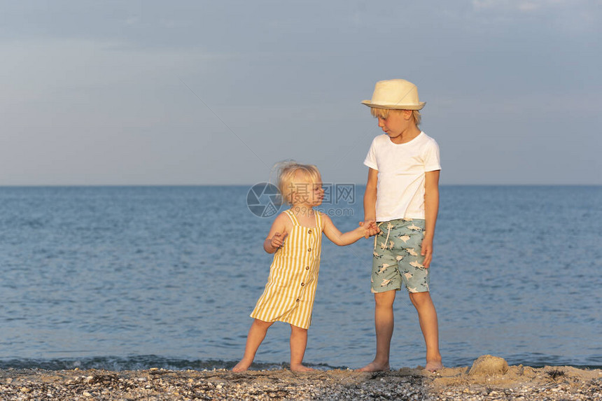 小兄弟和妹手牵沿着海岸走日落的光线图片