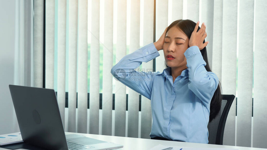 坐在办公室的亚裔妇女头痛所以她用手轻图片