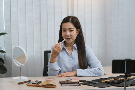 年轻的亚洲女在家里用手机摄像头为她的化妆品博客制作视频图片