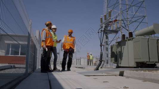 一群穿着背心和安全帽的同事在电站施工现场工作时使用平板电脑图片