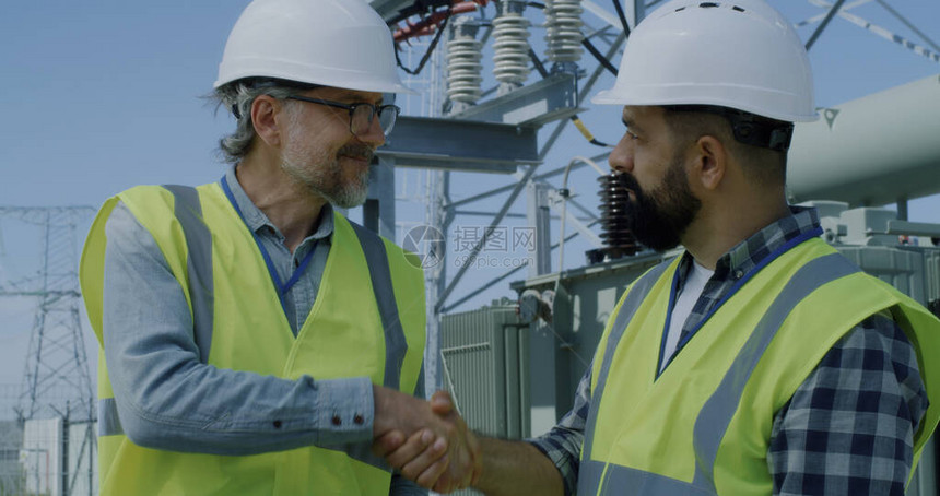 穿着背心和头盔的中年男子在风力发电站工作期间讨论平板上的数据图片