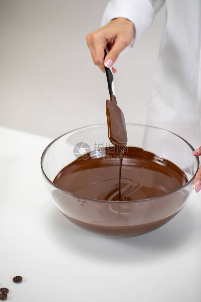 关闭搅拌和倾吐黑巧克力孤立在白色背景上Chocolatier制作优质的手工巧克力糖果制作糕点制作面包图片