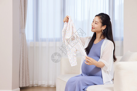 穿衣服的美女年轻居家孕妇手拿婴儿衣服背景