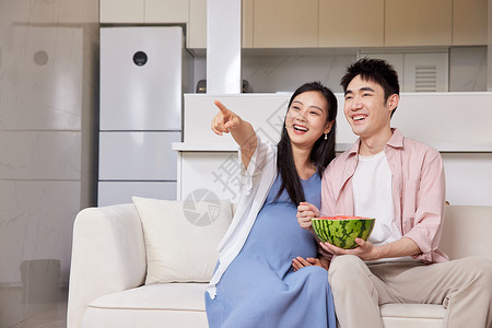 年轻待产的夫妻居家吃西瓜看电视背景