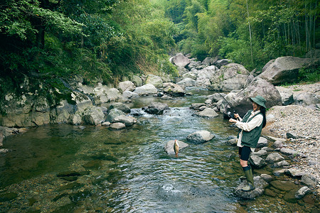 穿着蓑衣钓鱼青年女性溪流旁钓鱼背景