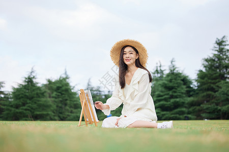 青年美女坐在草坪上绘画图片