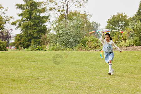 小女孩手拿风筝在草地上奔跑图片