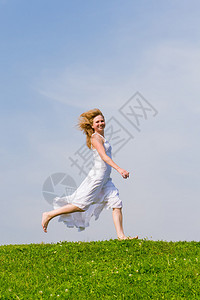 女孩在蓝天背景的草地上奔跑图片