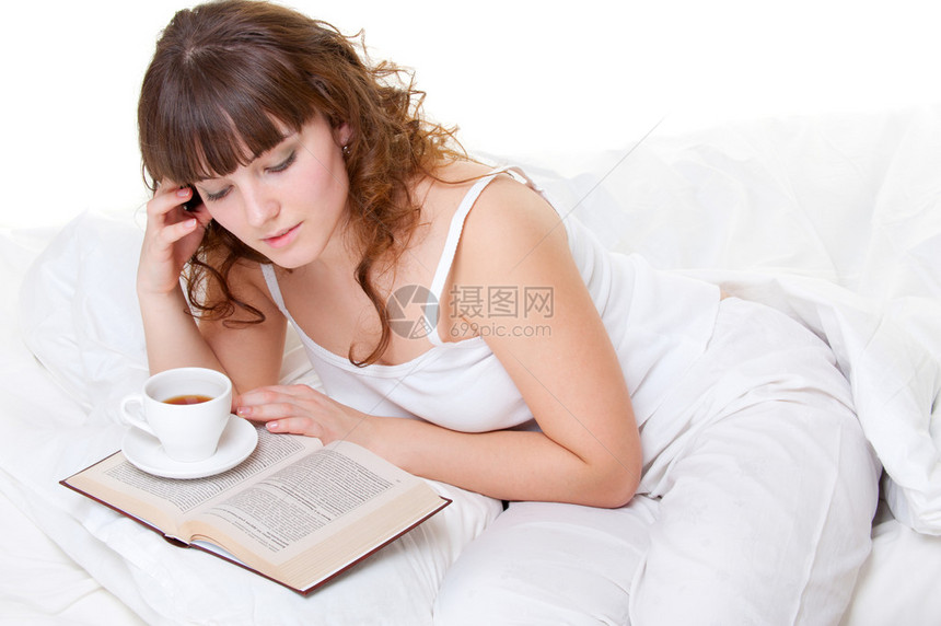 年轻女孩坐在床上拿着书和图片