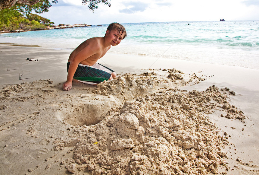 快乐的男孩正在建造一条运河从沙中流图片