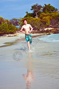 穿泳衣的红发小男孩在美丽的海滩上奔图片