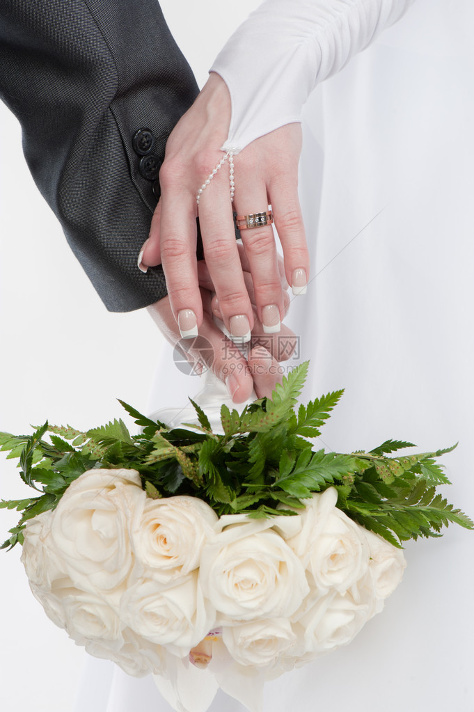 新郎和新娘的两只美丽的手带着结婚戒指和白玫瑰花图片