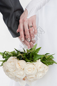 新郎和新娘的两只美丽的手带着结婚戒指和白玫瑰花图片