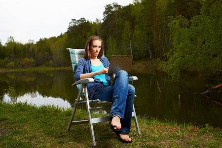 在森林池塘附近用笔记本电脑坐在折叠椅上的美图片