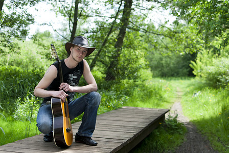 有吉他的人坐在树林里的桥上图片