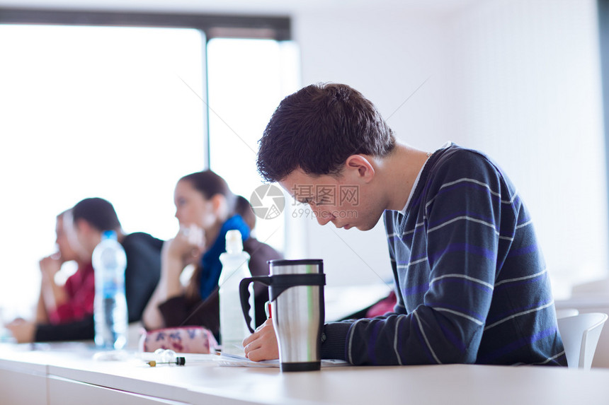 年轻英俊的男大学生上课时坐在满是学生的教室里图片