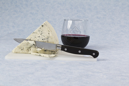 蓝色背景中的奶酪楔切刀红酒和切板图片