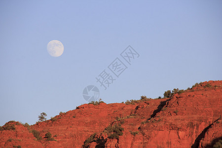 一轮满月从红色的岩石峭壁上升起图片