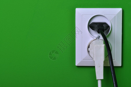 绿色墙上的电源插座中的电源线图片