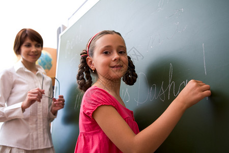 在黑板上写作的聪明女学生与背景老师的照片图片