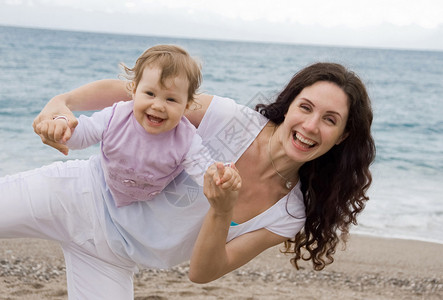 快乐的女在海边和可爱的婴儿玩耍都笑了图片