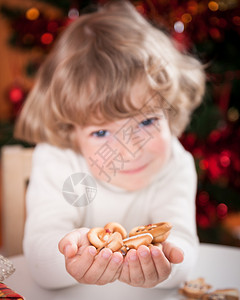 快乐的孩子拿着饼干在圣诞节的灯光背图片
