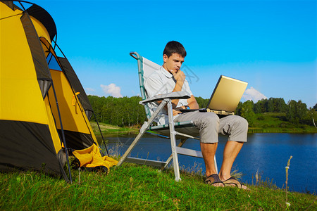 在露营帐篷室外附近用笔记本电脑坐在折叠椅上的人图片