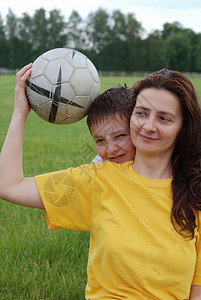 穿着黄衬衫的笑女人拿着橄榄球十二岁的男孩从后面偷溜出来绿色草图片