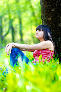 穿着牛仔裤和T恤的美丽的黑发美女夏天坐在一棵树图片