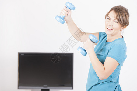 妇女在家里使用屏幕电视指示用哑铃做背景图片