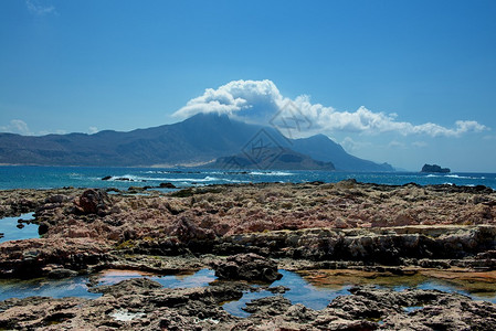 在希腊小岛的岩石海岸上与海浪交锋在地平线上有白云图片