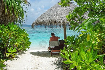 坐在雨伞下的人坐在美丽的沙滩上图片