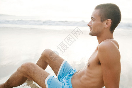 一个年轻人坐在海边的近距离肖像日落时图片