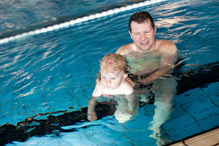 父亲和男婴在室内游泳池里游泳图片