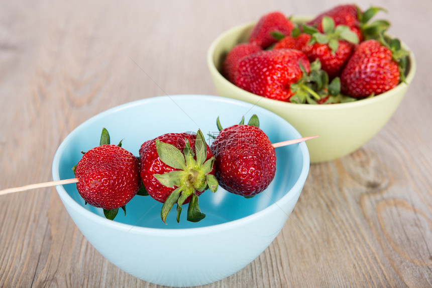 在五颜六色的碗里的新鲜成熟的草莓木制背景图片