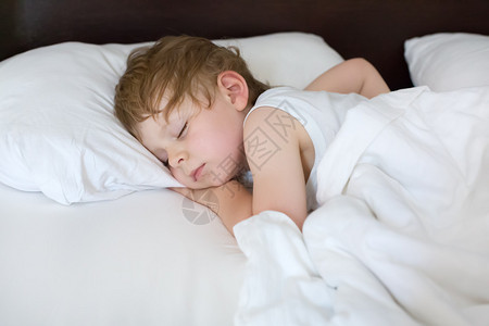 甜蹒跚学步的小男孩在他的床上睡觉图片