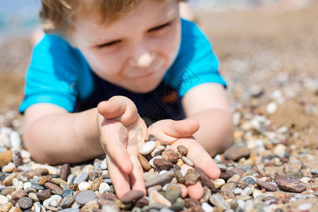 蹒跚学步小男孩玩沙子和石头在沙滩上图片