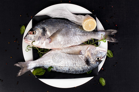 两条新鲜的海鲜鱼在盘子上配有新鲜草药迷迭香切柠檬和多彩的胡萝卜图片