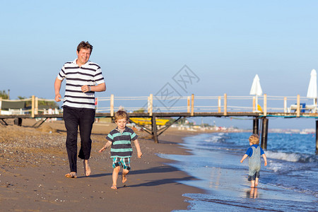快乐的父亲和两个小男孩在海滩图片