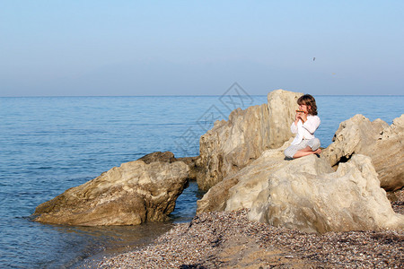 小女孩坐在海边的岩石图片