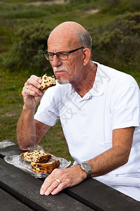 有胡子和眼镜的退休男子在草地上休息和吃午饭图片