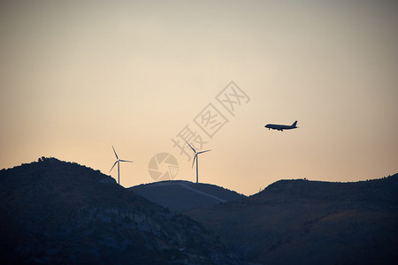 飞机在山景中飞过风力涡轮机图片