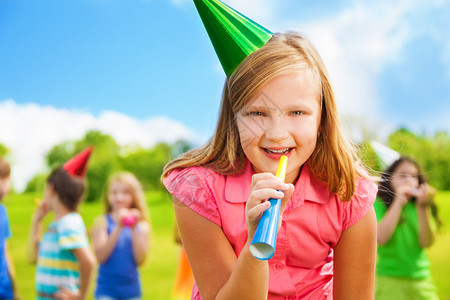 快乐女孩的肖像与噪音制造者吹口哨在生日派对上穿着帽子和朋图片