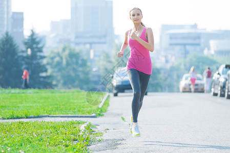 在美丽的夏日阳光下在城市公园奔跑的慢跑妇女图片